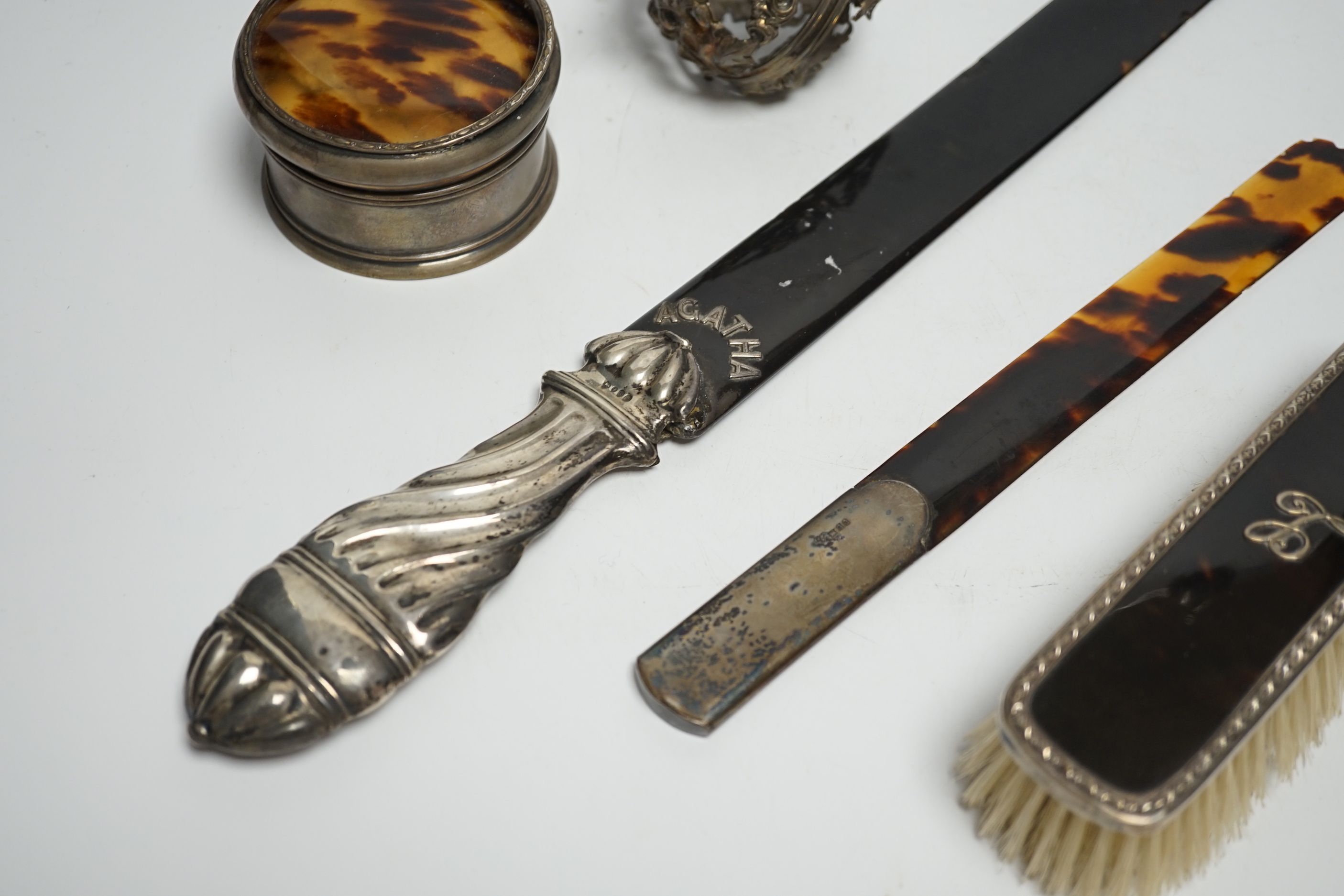 A late Victorian silver handled tortoiseshell page turner, a small page turner, a silver and tortoiseshell box and brush and a white metal pomander case.